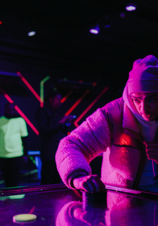 Someone playing air hockey in BOXPARK Wembley with a neon pink light in the left hand side.