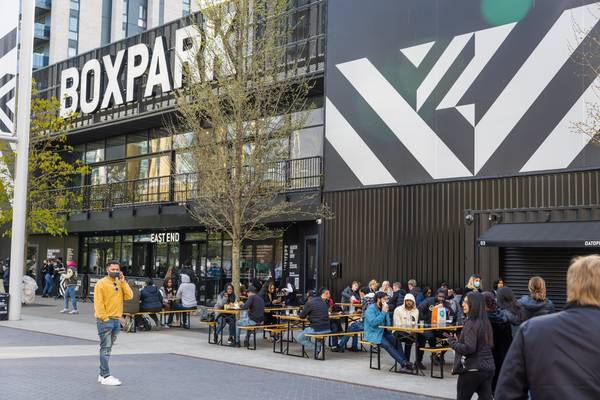 BOXPARK Wembley food and entertainment venue with outdoor seating area showing people dining al fresco, the BOXPARK sign, and East End entrance, withi