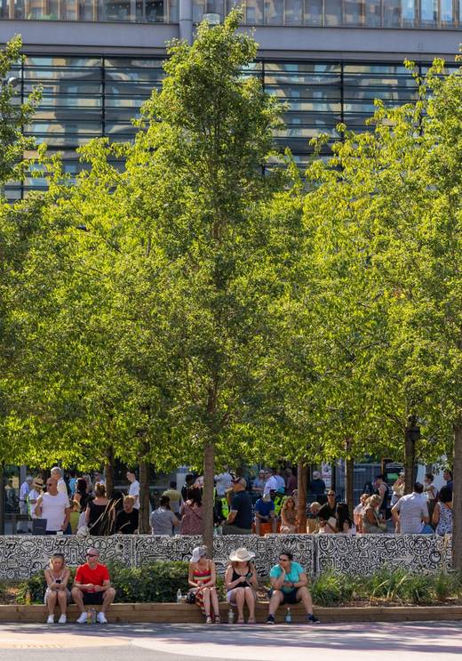 Summer crowds relaxing at Mr Doodle-decorated benches under leafy trees on Olympic Way at Wembley Park for the FA Cup Final 2026