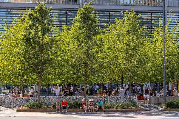 Summer crowds relaxing at Mr Doodle-decorated benches under leafy trees on Olympic Way at Wembley Park for the FA Cup Final 2026