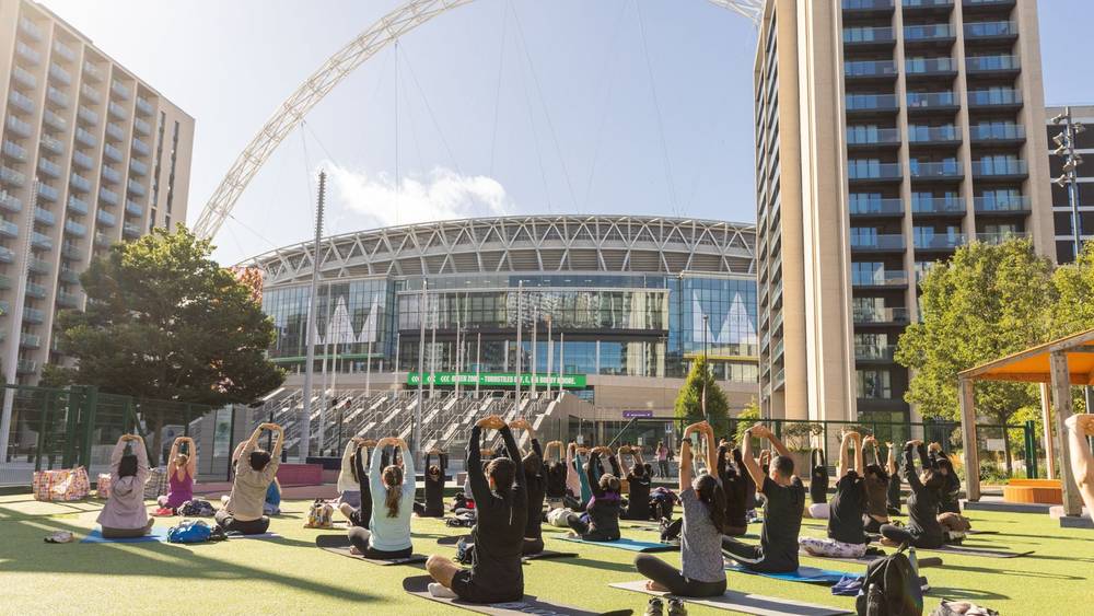 Residents taking part in an outdoor wellness session in Market Square at Wembley Park, with Wembley Stadium in the background