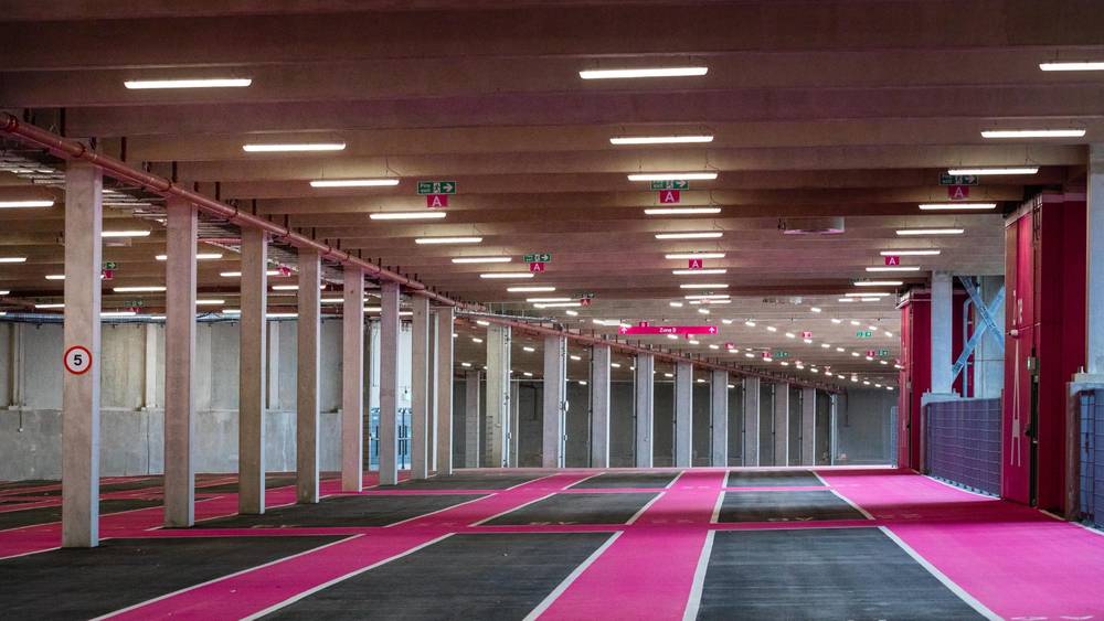 Interior of Pink Parking at Wembley Park showing Zone A and Zone B wayfinding signage, fire exit signs, speed limit sign, rows of spacious parking bay