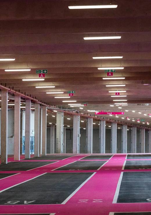 Interior of Pink Parking at Wembley Park showing Zone A and Zone B wayfinding signage, fire exit signs, speed limit sign, rows of spacious parking bay