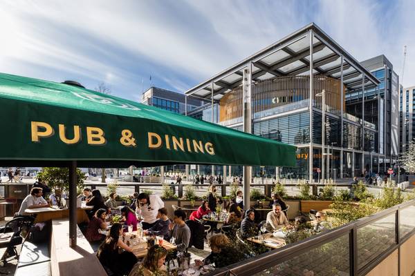 Outdoor pub and dining terrace at Wembley Park showing people enjoying al fresco meals under a green Pub and Dining canopy with the Wembley Library bu