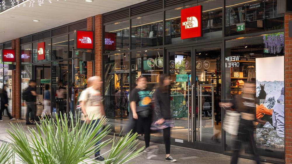The North Face outlet store shopfront at London Designer Outlet, Wembley Park, with red logo signage and shoppers passing the glass entrance.