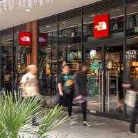 The North Face outlet store shopfront at London Designer Outlet, Wembley Park, with red logo signage and shoppers passing the glass entrance.