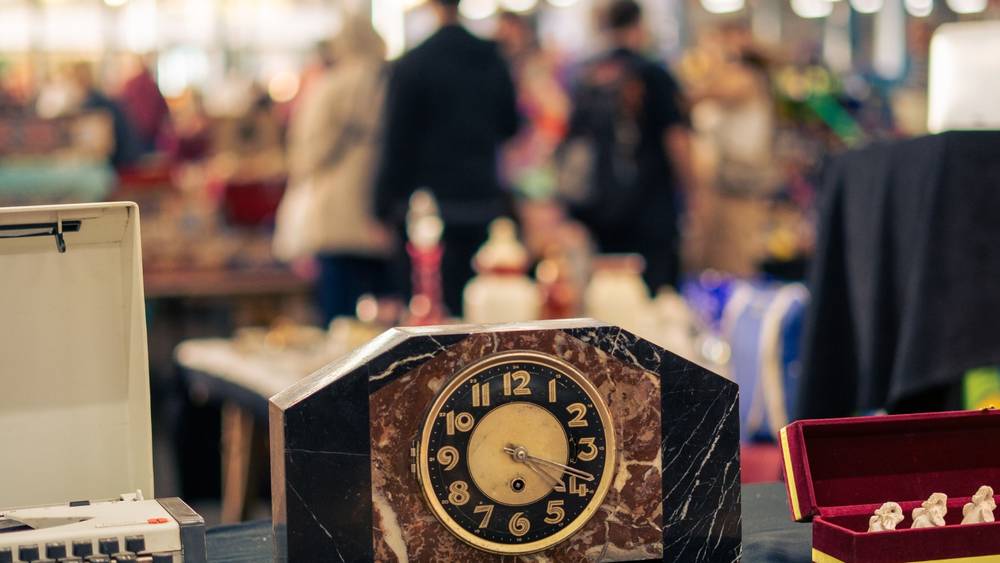 An art deco style marble mantel clock on a stall table, with shoppers browsing behind