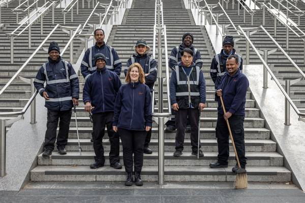 Wembley Park's cleaning team in navy uniforms and hi-vis jackets on the Olympic Steps, Carla Martins at the front and a team member holding a broom