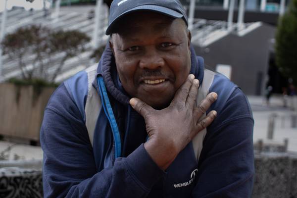 Mallan Falconer of Wembley Park's cleaning team, smiling, in a Wembley Park cap, resting his chin on his hand