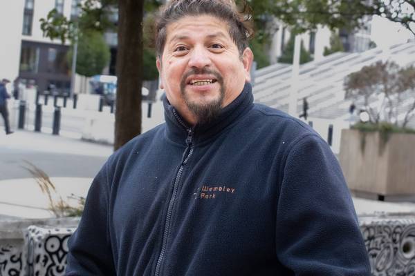 Edward Espinoza of Wembley Park's cleaning team, smiling, in a navy Wembley Park fleece, in front of patterned public seating