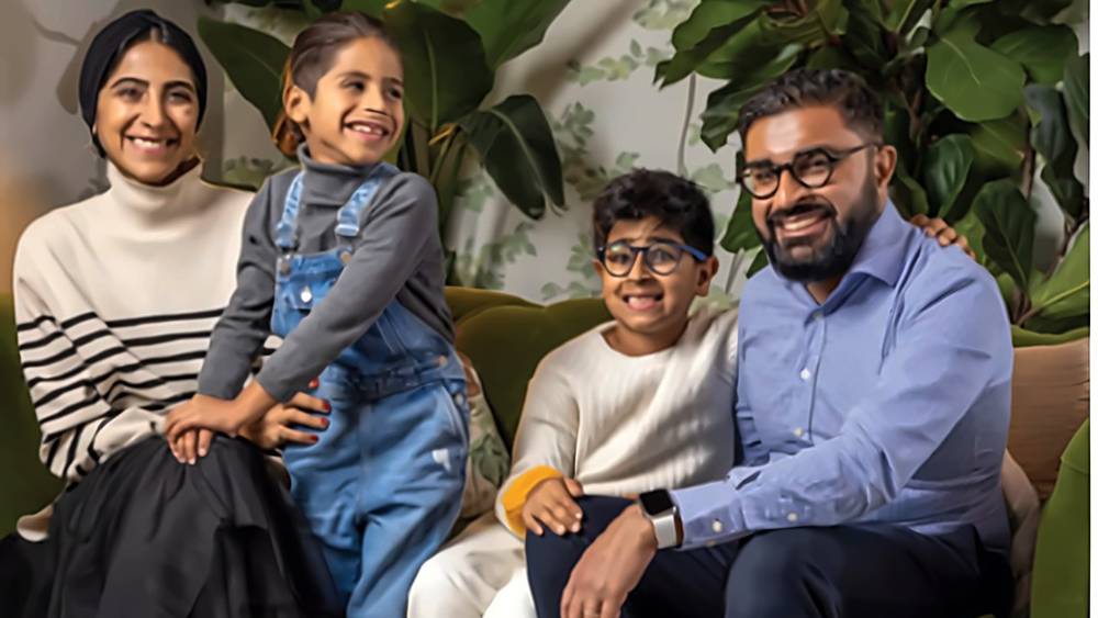 The Jetha family, Shamir, Reschma and their two sons, smiling together on a green velvet sofa surrounded by plants at home in Alameda, Quintain Living