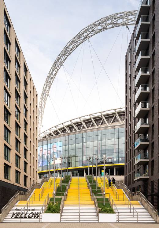 Full view of YELLOW 25 by Wembley Park x Pantone on the Spanish Steps, celebrating 25 years of Coldplay’s Yellow, with Wembley Stadium arch in the bac